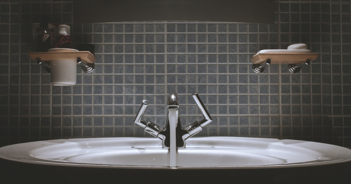 water faucet running in a tiled bathroom sink