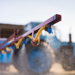 arm of a tractor fitted with a spray nozzle being used to disperse pesticides on a farm field