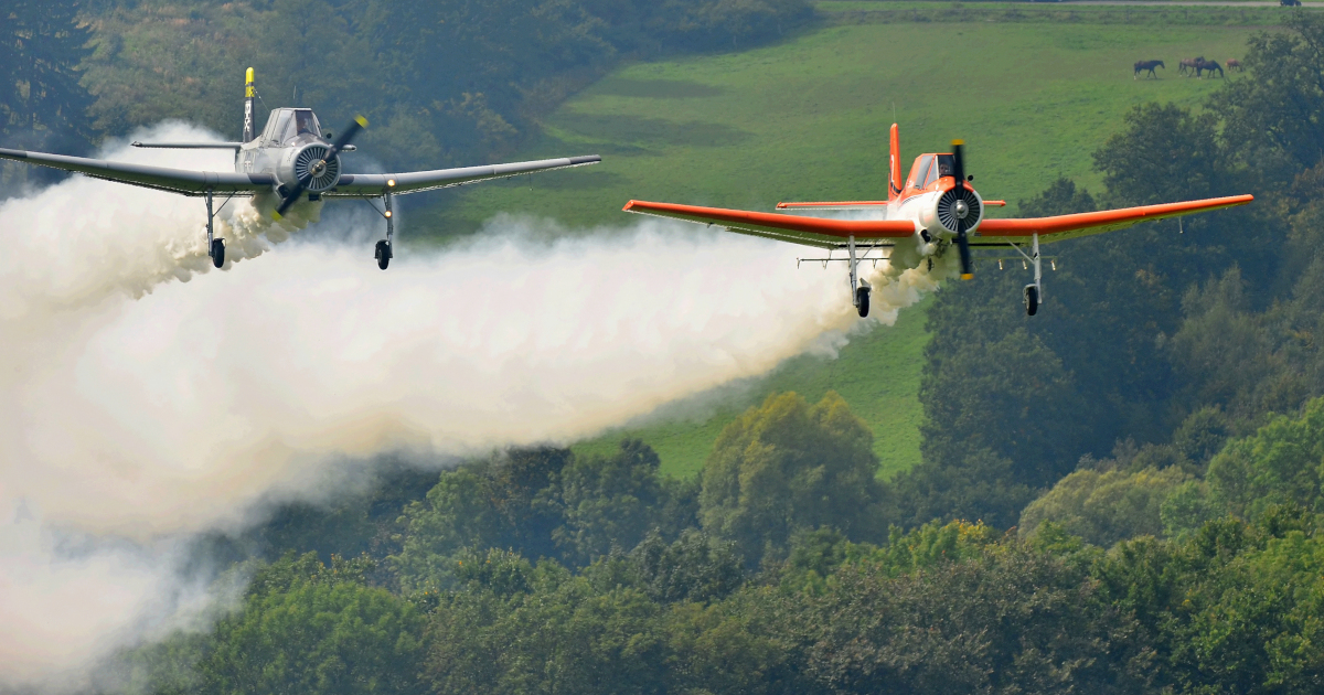 two crop duster airplanes spraying pesticides over a farm field