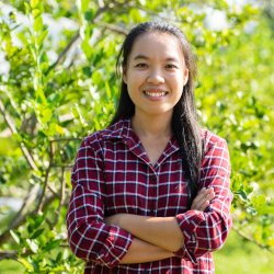 smiling farmer standing in a lime garden in a plaid shirt with her arms crossed