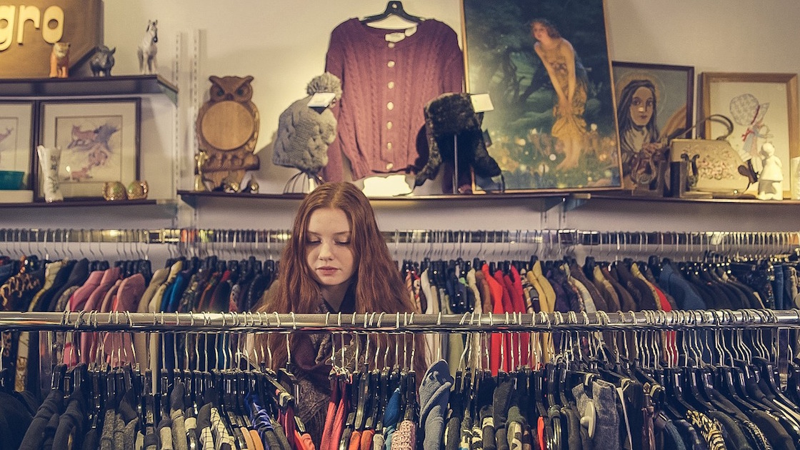 girl looking through clothes rack while shopping
