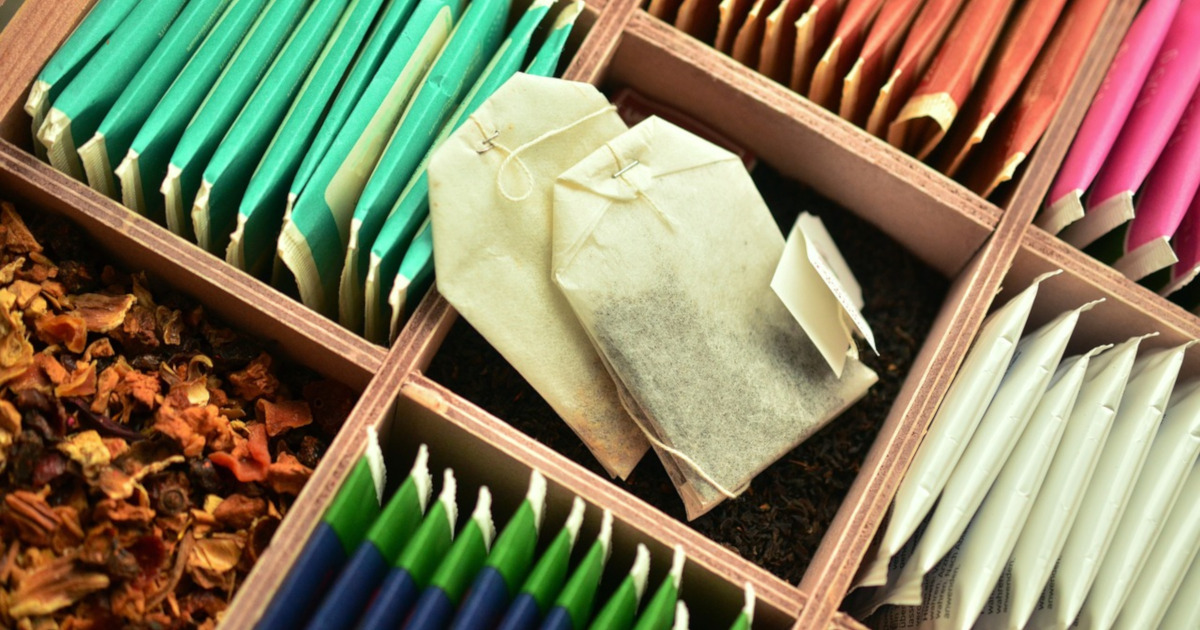 opened packages of tea bags sitting in a wooden container along with a section of loose leaf tea