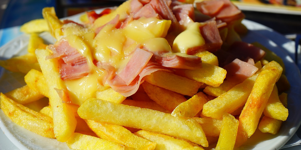 french fries on a plate with processed meat covered with melted cheese