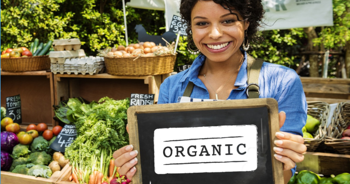 woman at a farmers market holding a sign reading ORGANIC