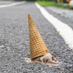 chocolate ice cream in a waffle cone dropped on an asphalt road