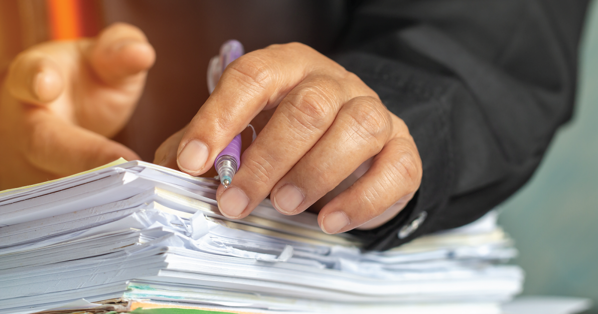 Person with hands and pen on a pile of documents.