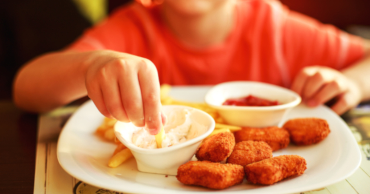 young boy eating chicken nuggets with sauces