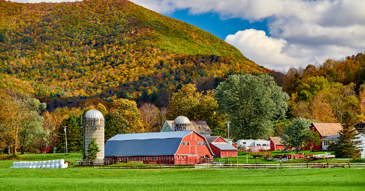 red barn and silo on a farm field beside a mountain landscape