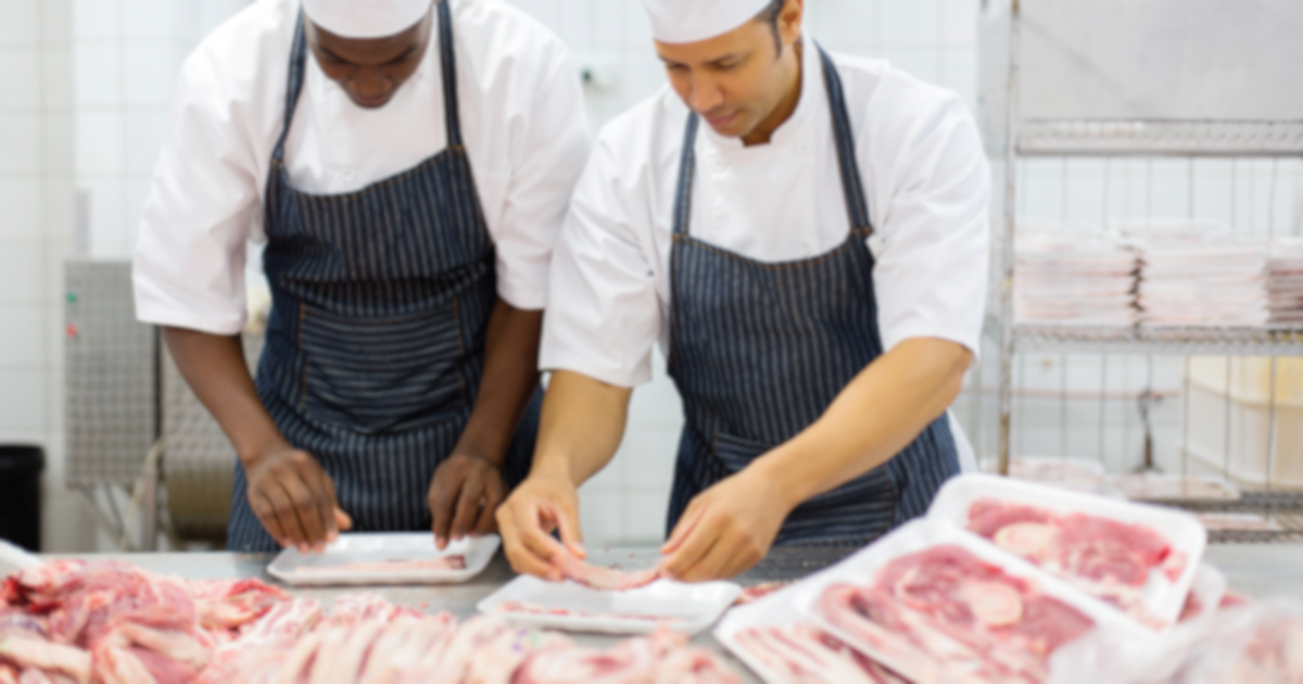 two butchers in black and white striped aprons and hats cutting meat in a slaughter house