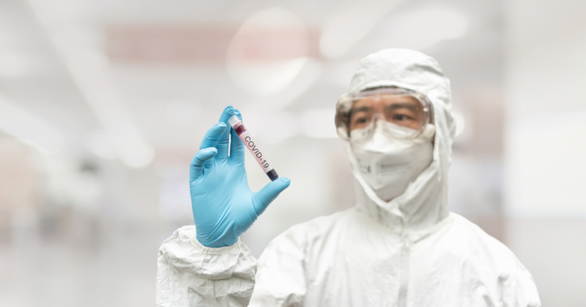 scientist in a white hazmat suit holding a test tube of coronavirus blood sample