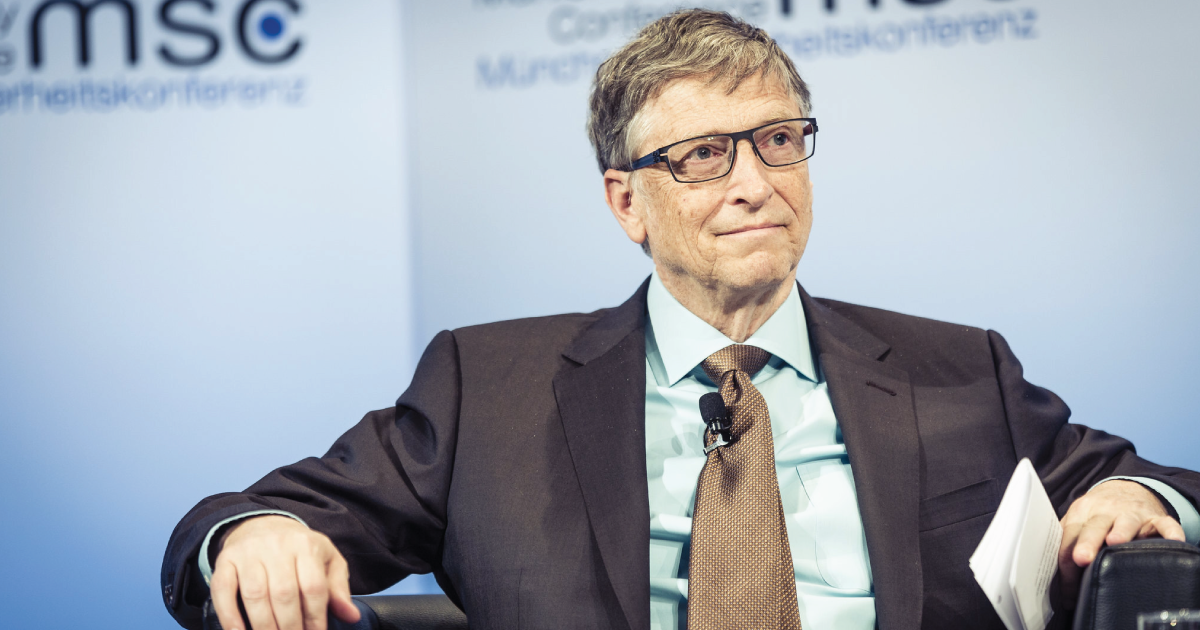 Photograph of Bill Gates sitting in a chair in a suit with a blue background