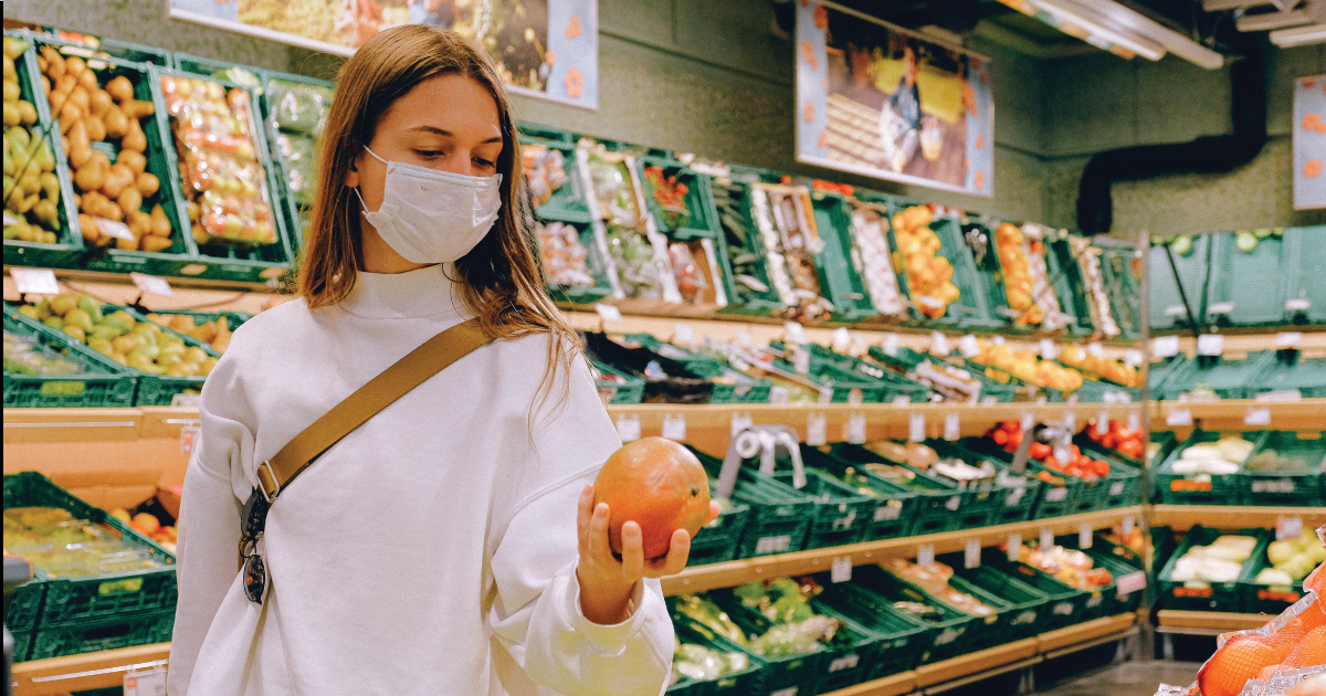 Masked woman shopping for food, holding a grapefruit.