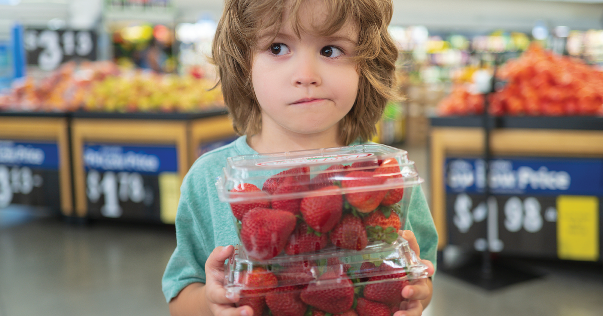 Child with strawberries in plastic packaging.