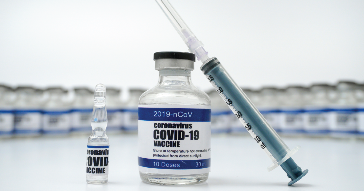 A photograph of a covid-19 vaccine in a bottle with an injection needle leaning on it.