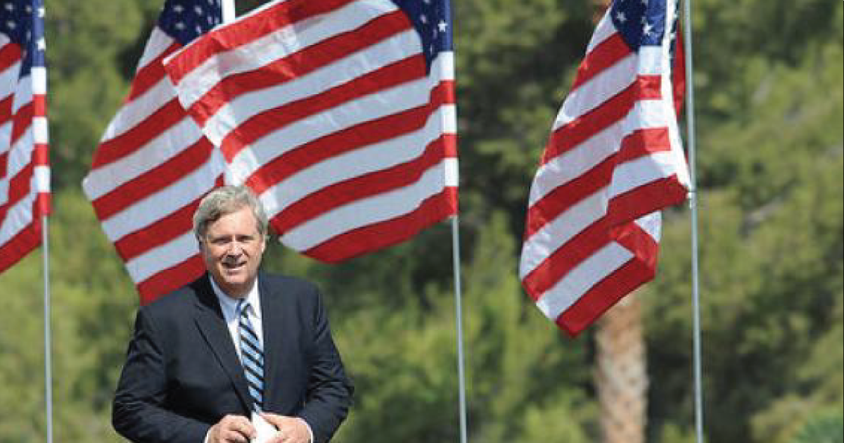 Tom Vilsack in front of some American flags.