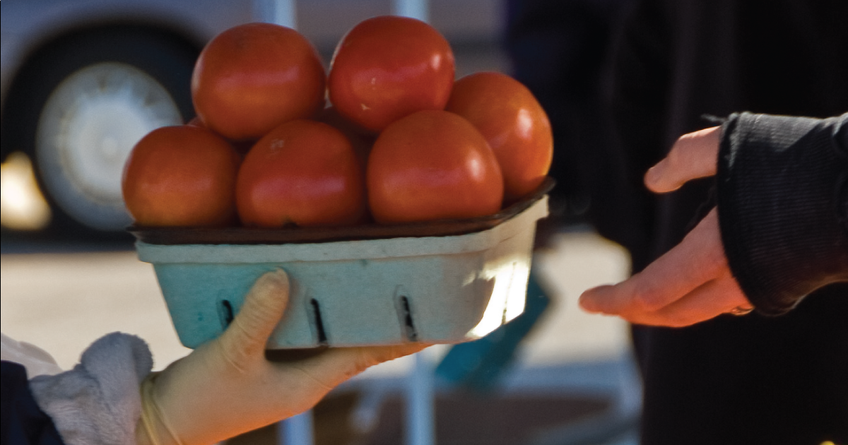 Someone buying tomatoes at a farmers market.