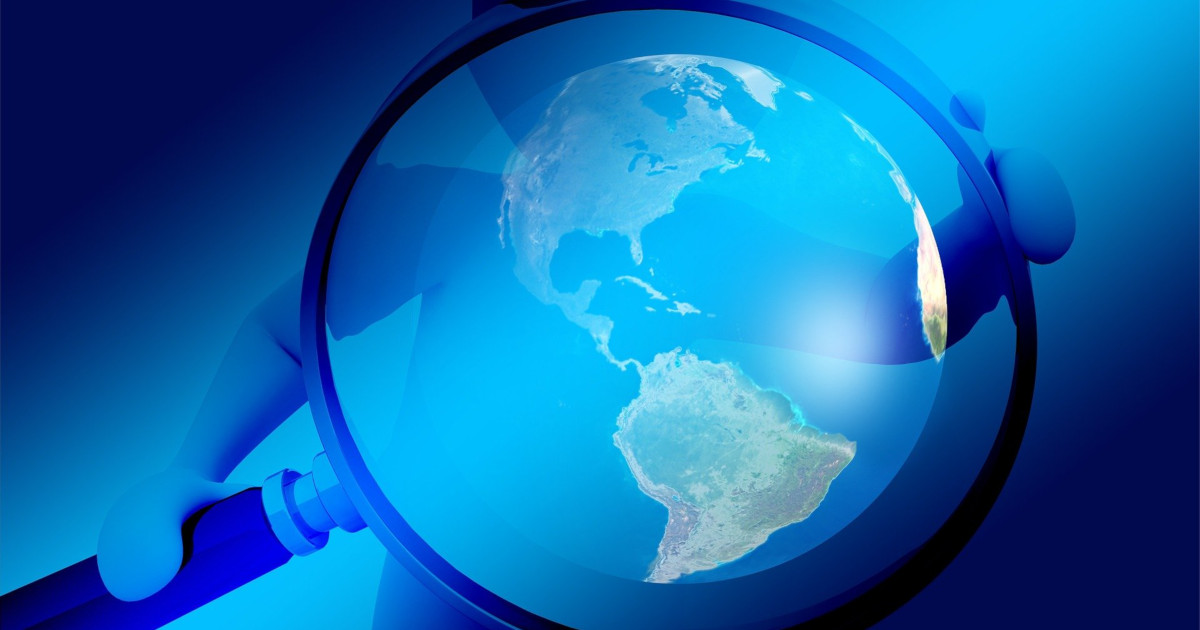 Person holding a magnifying glass over blue earth
