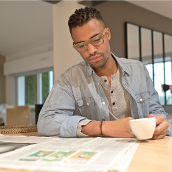 man reading a newspaper at a table with a cup of coffee