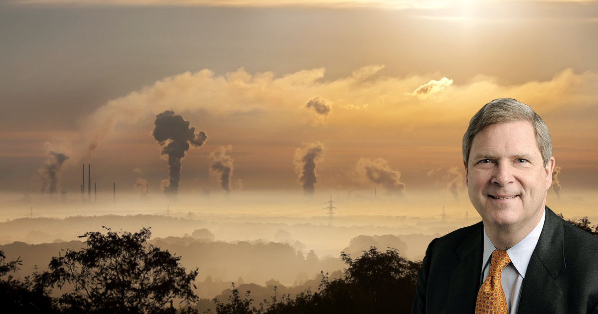 Tom Vilsack against a factory spewing pollution into the air