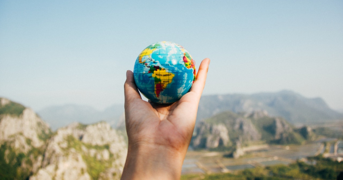 hand holding a small world globe against a mountain landscape